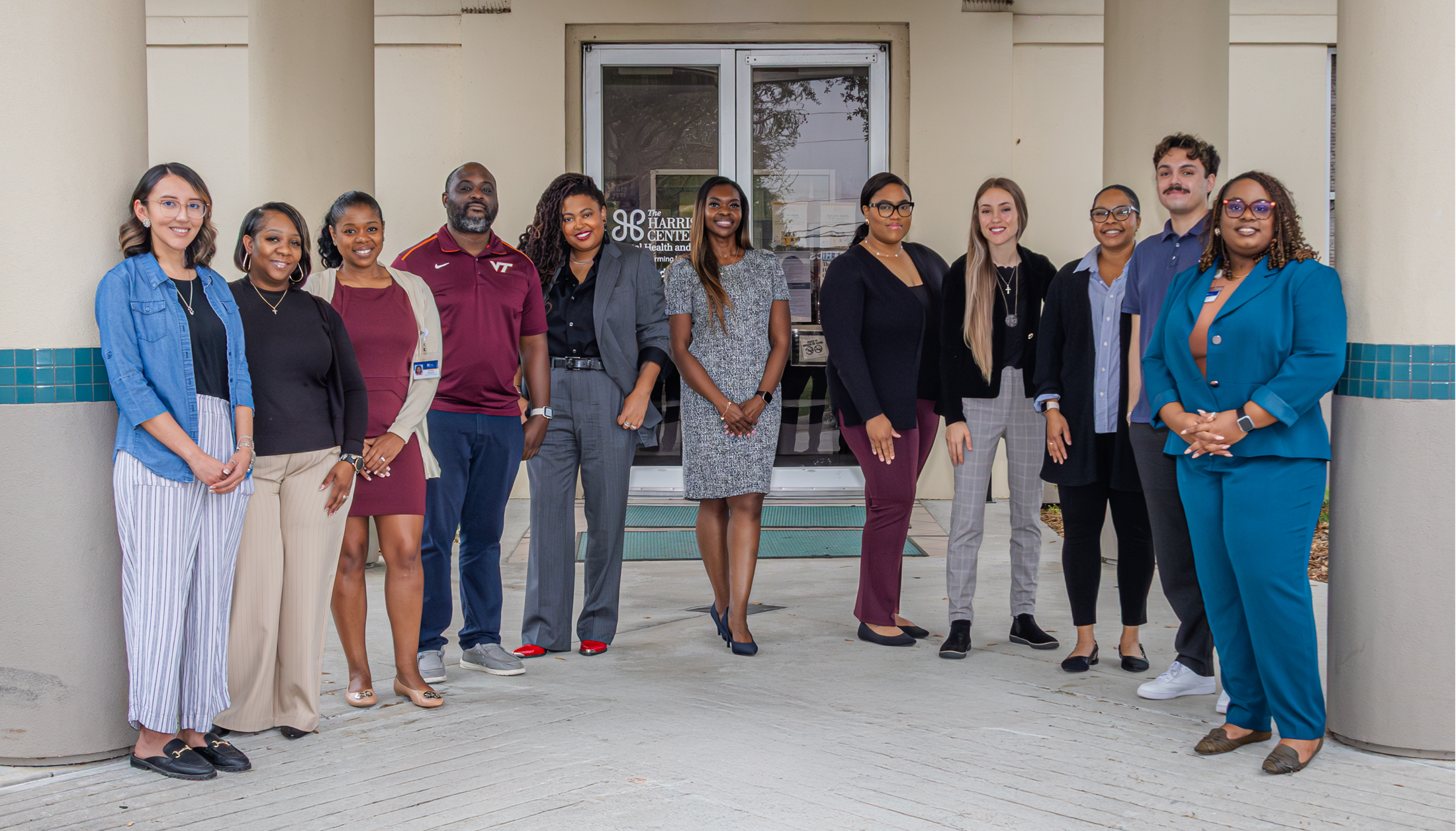 Group of professionally dressed individuals standing and smiling in front of The Harris Center building entrance.
